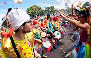 pessoas vestidas com fantasia de carnaval coloridas, tocando instrumentos de percussão, desfilando nas ruas de São Paulos dentro de bloco de rua de carnaval.